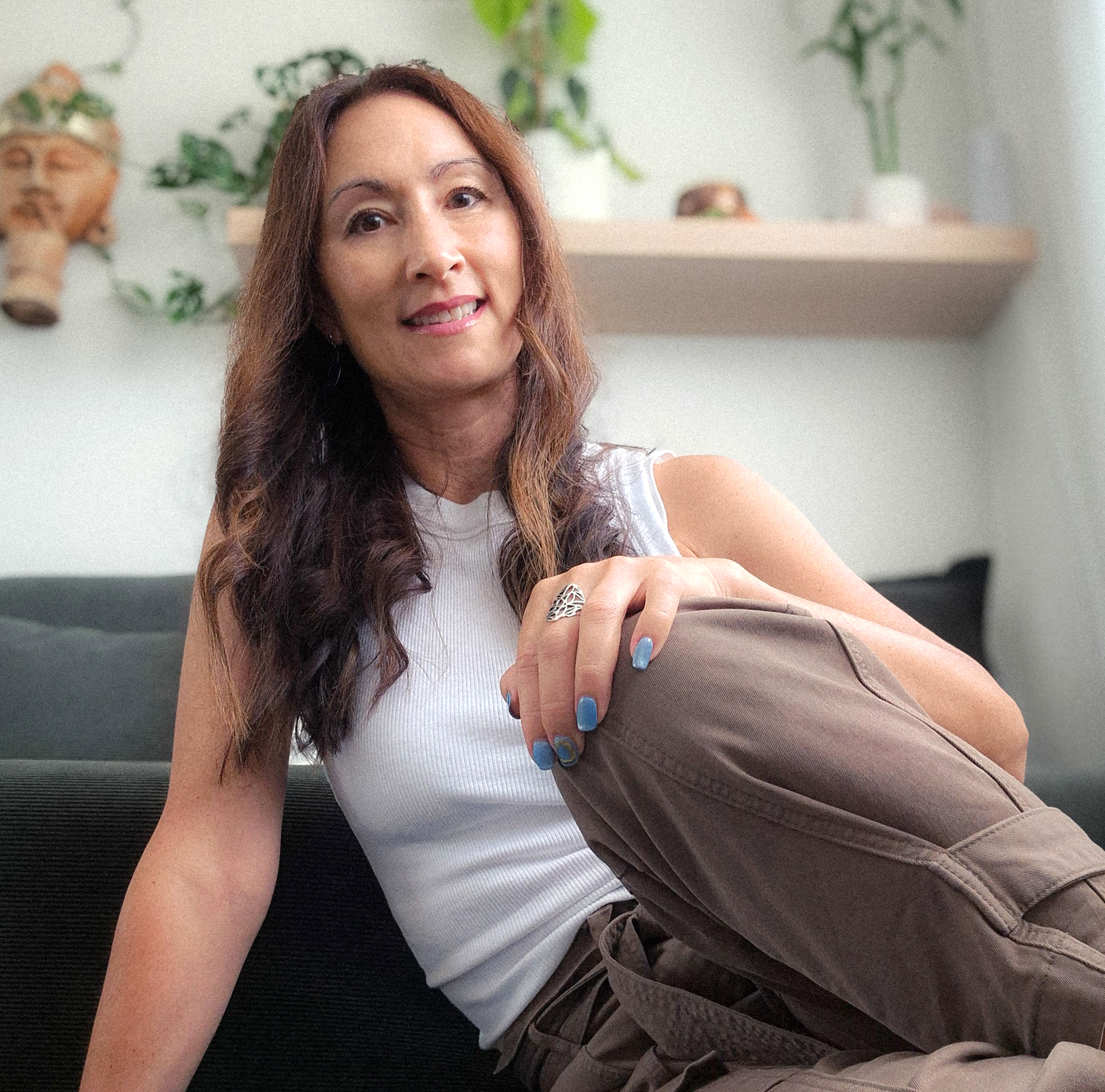 Dark haired woman leaning on one arm and smiling at the camera in a relaxed setting
